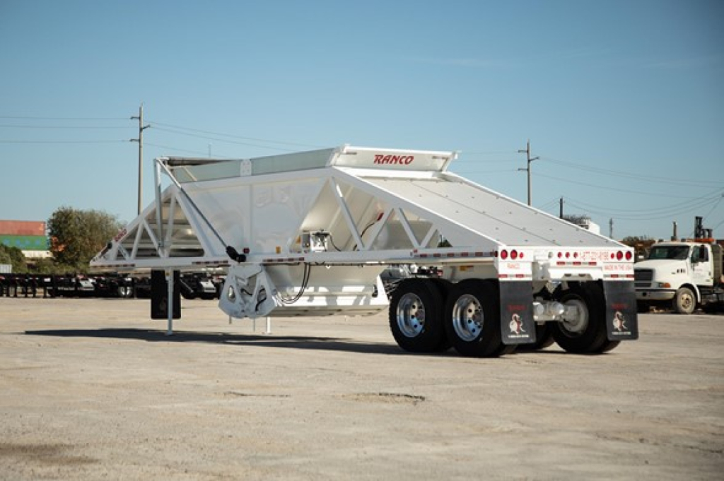 Ranco Wet Sand Switchgate Bottom Dump trailer in a yard, white with red RANCO logo on upper frame, triple-axle wheels, side panels, rear lights.