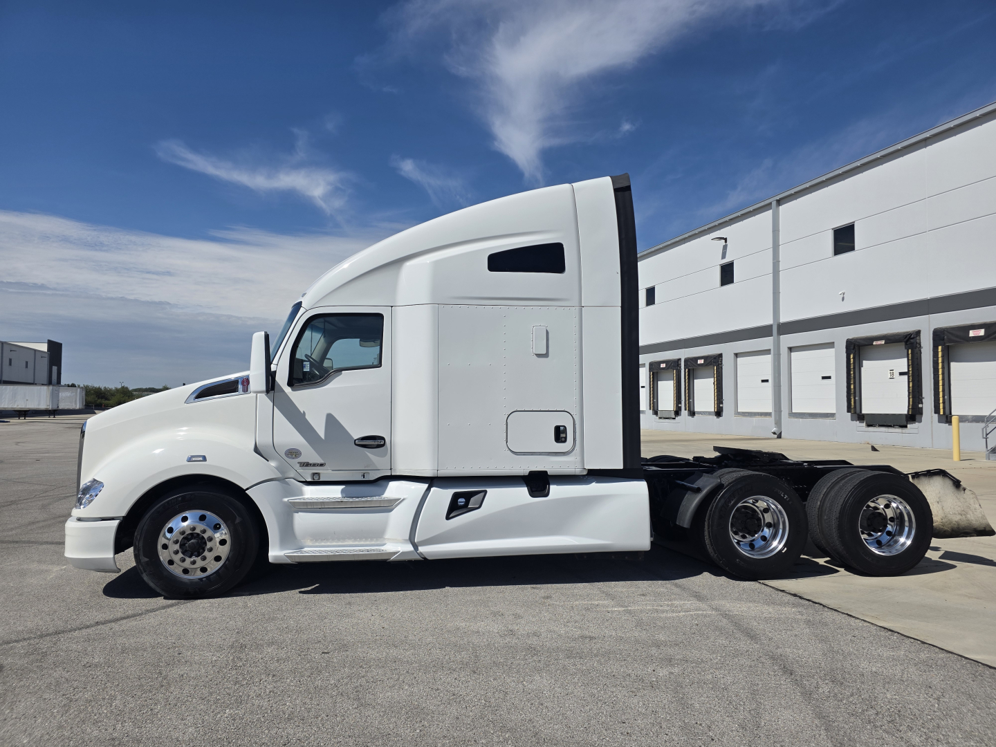 Side view of a white 2022 Kenworth T680 conventional sleeper truck with three rear axles and chrome wheels.