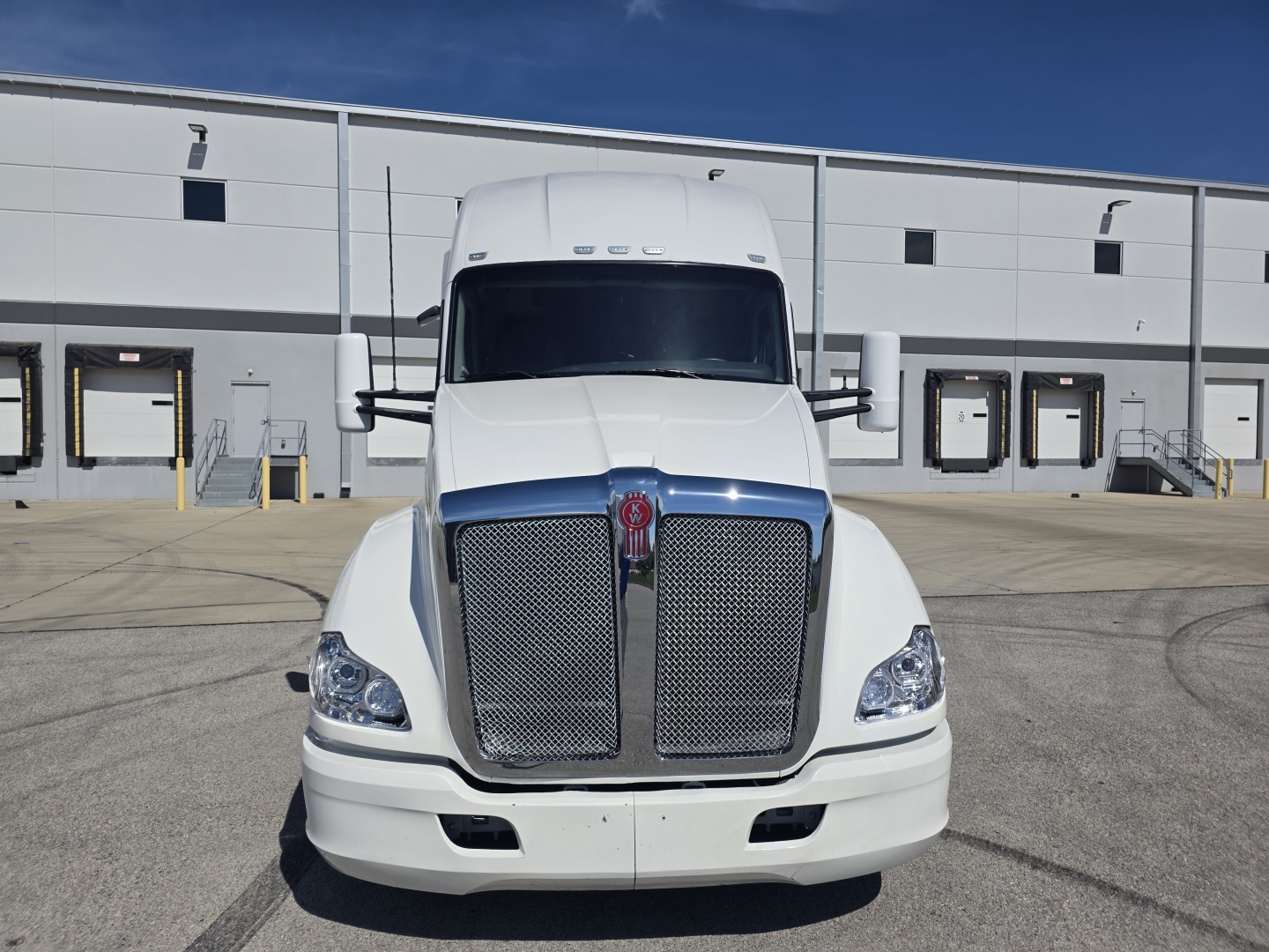 Kenworth T680 front view showing large chrome grille and headlights in a loading area.