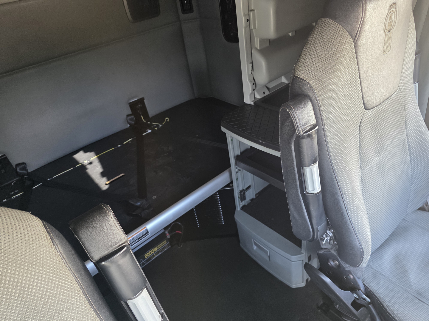 Kenworth truck cab interior showing seating and storage area with a metallic rail and steps, no readable text present.