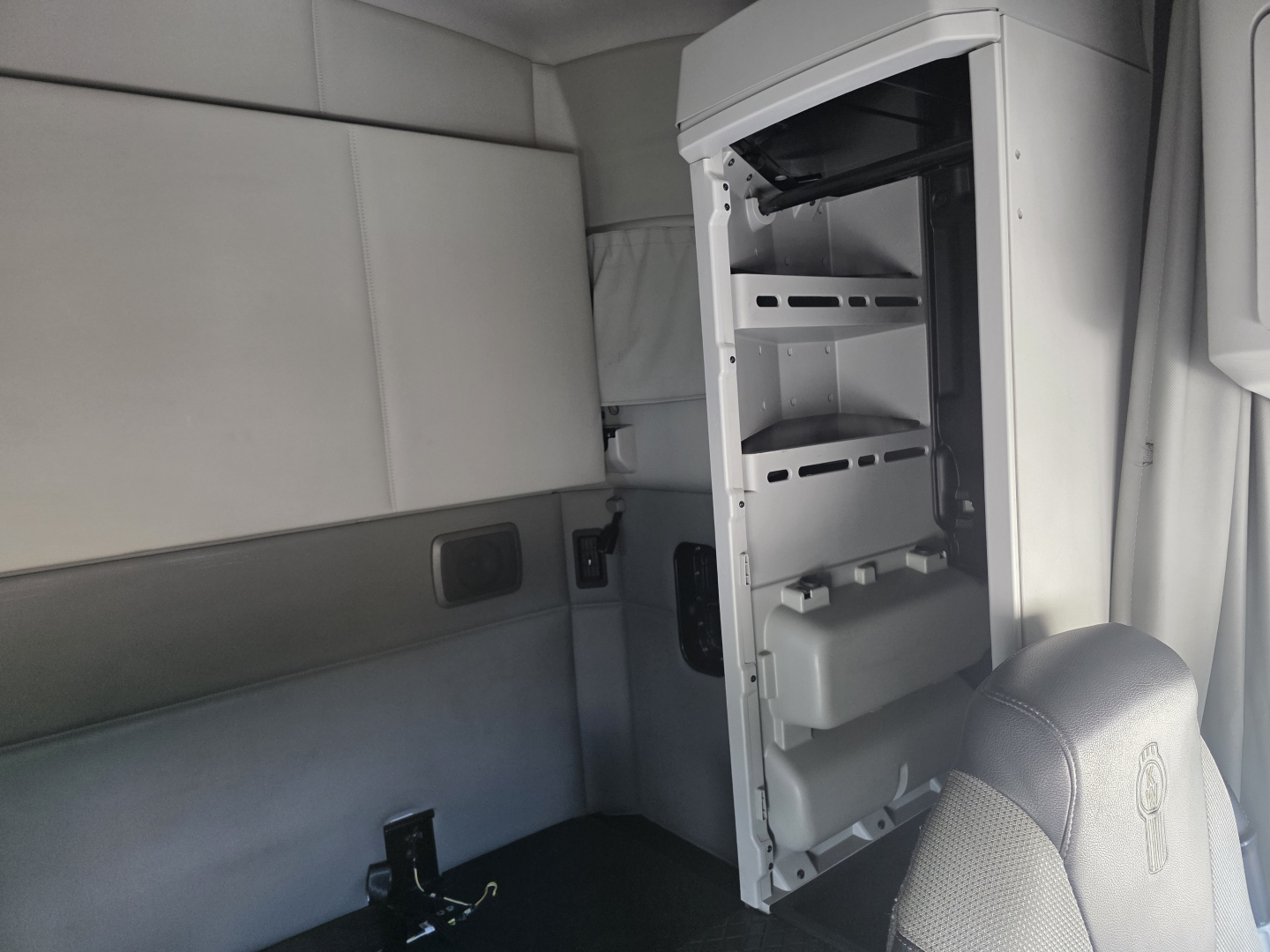 Interior of Kenworth T680 cab showing open refrigerator/mini-bar with shelves and storage compartments on a light gray interior.
