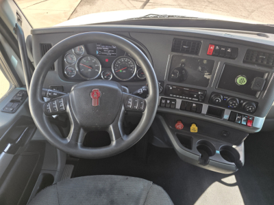 Kenworth T680 cockpit/dashboard view showing steering wheel, gauges, switches, and gear area.