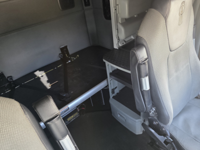 Kenworth truck cab interior showing seating and storage area with a metallic rail and steps, no readable text present.