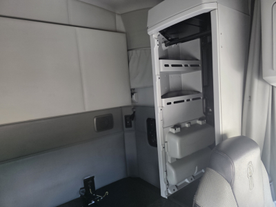 Interior of Kenworth T680 cab showing open refrigerator/mini-bar with shelves and storage compartments on a light gray interior.