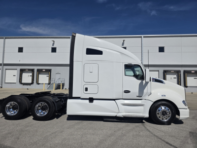 Kenworth T680 tractor side view showing sleeper cab, white paint, chrome wheels, and fuel tanks. No readable text or labels visible on the side.