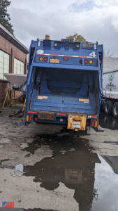 Rear view of a blue 2013 Mack LEU 613 trash truck showing rear hopper and taillights.