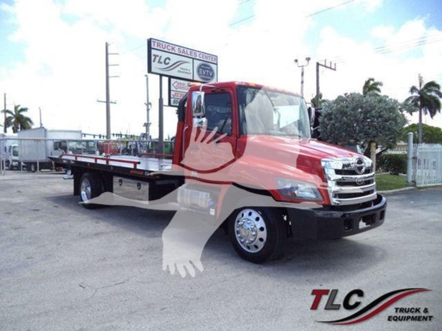 2020 Hino 268A rollback truck with red cab and flatbed, front grille visible, TLC Truck Sales Center sign in background.