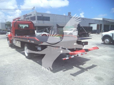 Tow truck rollback with red cab and black flatbed in a dealership lot showing Hino 268A features and rear towing apparatus.