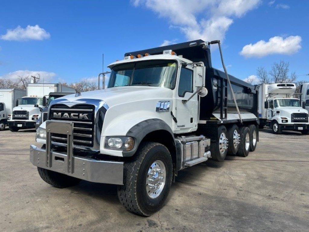 Dump truck showing Mack GU713 front and side view with white cab and gray dump body.
