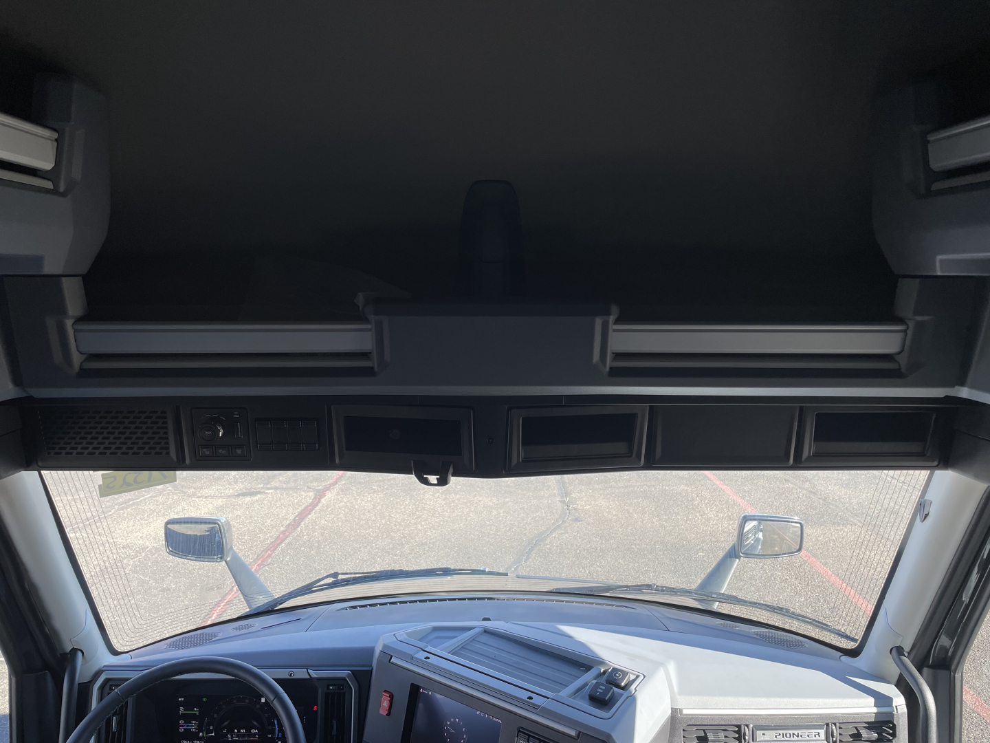 Truck cab interior forward view through windshield showing dash controls and sleeper overhead storage; Mack PR64T76H listing image.
