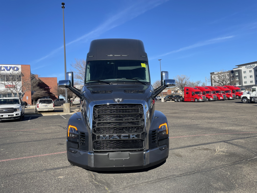Front view of a dark gray Mack PR64T76H tractor sleeper cab truck, large grille with Mack logo, headlights, chrome mirrors, daytime running lights.