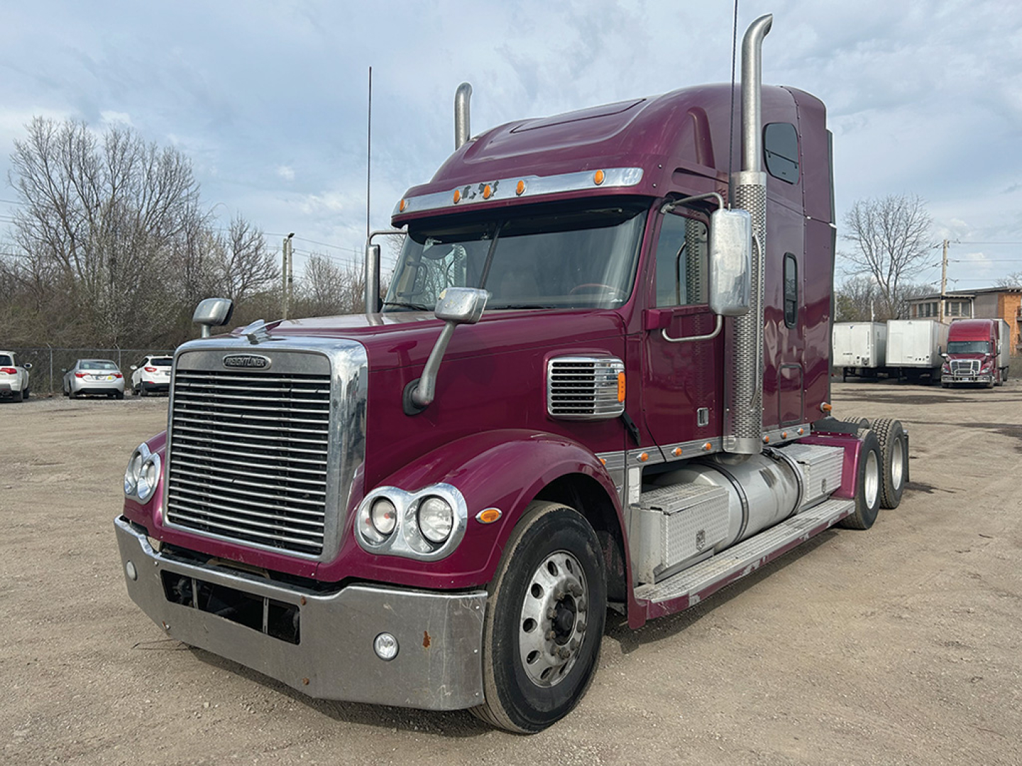 Conventional sleeper truck cab showing front grille, maroon paint, chrome bumper, dual exhaust stacks, and side fuel tanks.