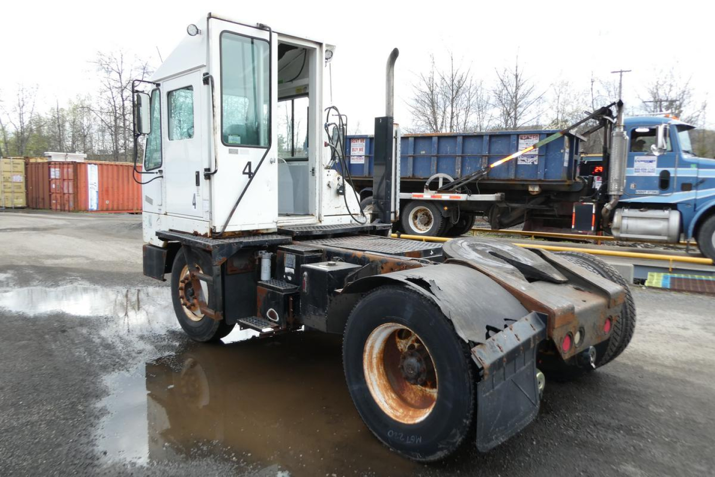 Truck chassis with white cab and 4X2 badge showing rear dual wheels and lifted cab in a yard.