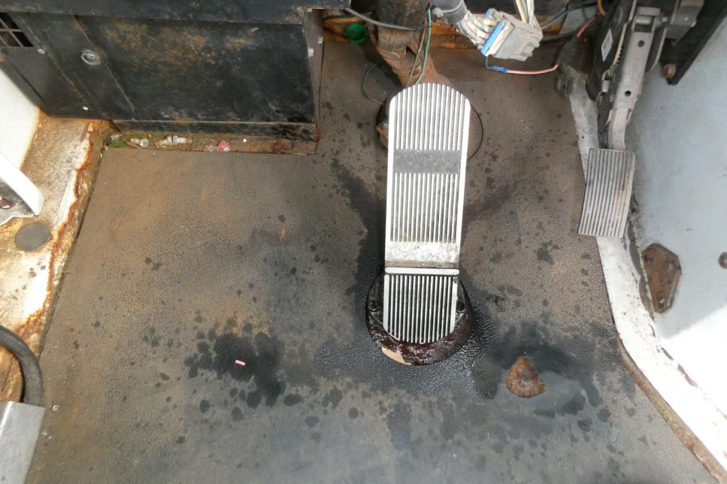 Pedals and floormat area of a truck cab showing accelerator and brake pedals with wiring and metal floor during inspection.