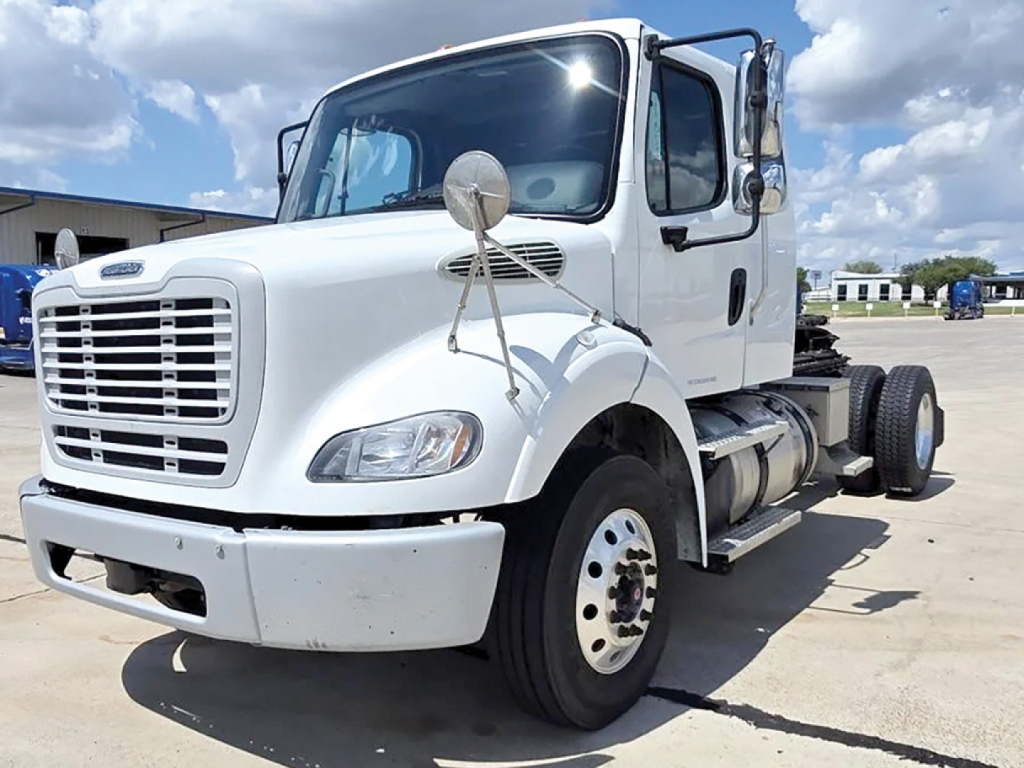 Freightliner M2 112 extended cab truck in white, front-left view showing grille, bumper, dual mirrors, and side fuel tank.
