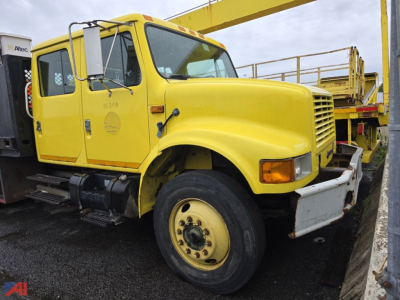 International 4700 flatbed truck in yellow seen from front-left; visible text on door and grille area, no detailed labels legible.