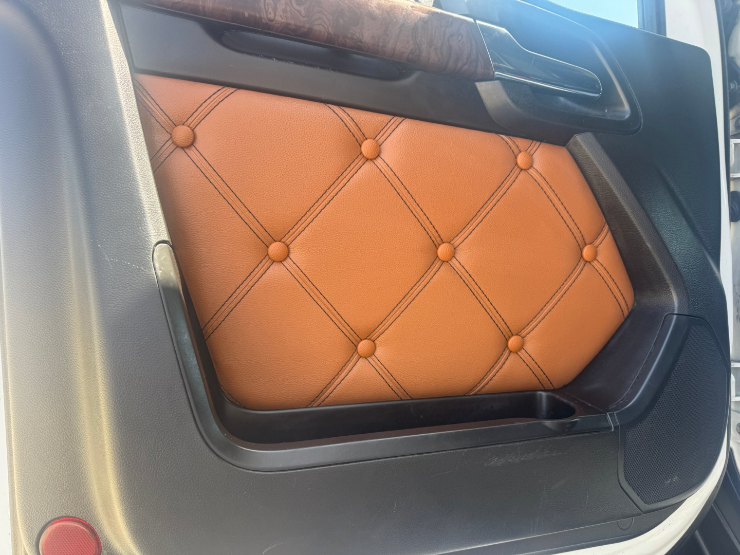 Truck interior door panel with orange diamond-stitched leather insert in Kenworth T680 cab interior.