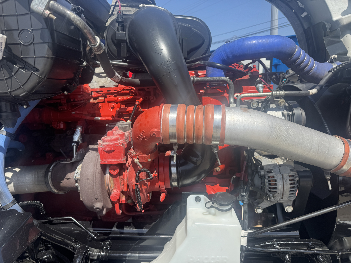 Kenworth T680 engine bay showing red engine components with hoses and a large gray intake pipe.