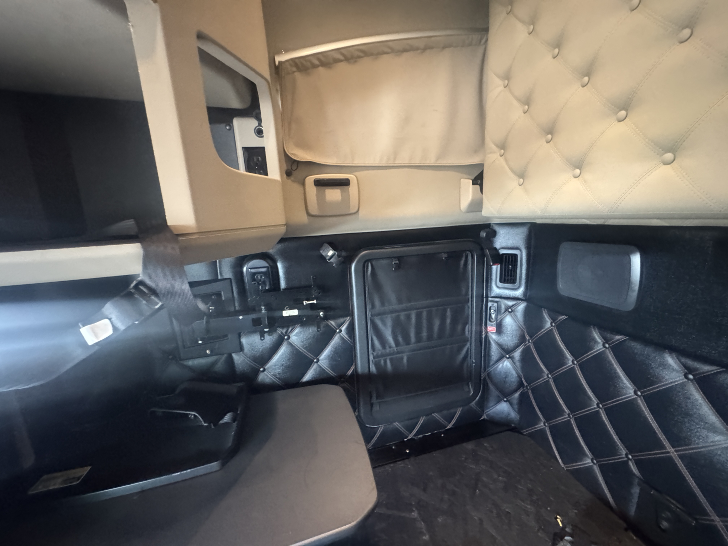 Kenworth T680 interior cab area with quilted black storage panels and beige sleeping area, dashboard edge visible, no readable labels.