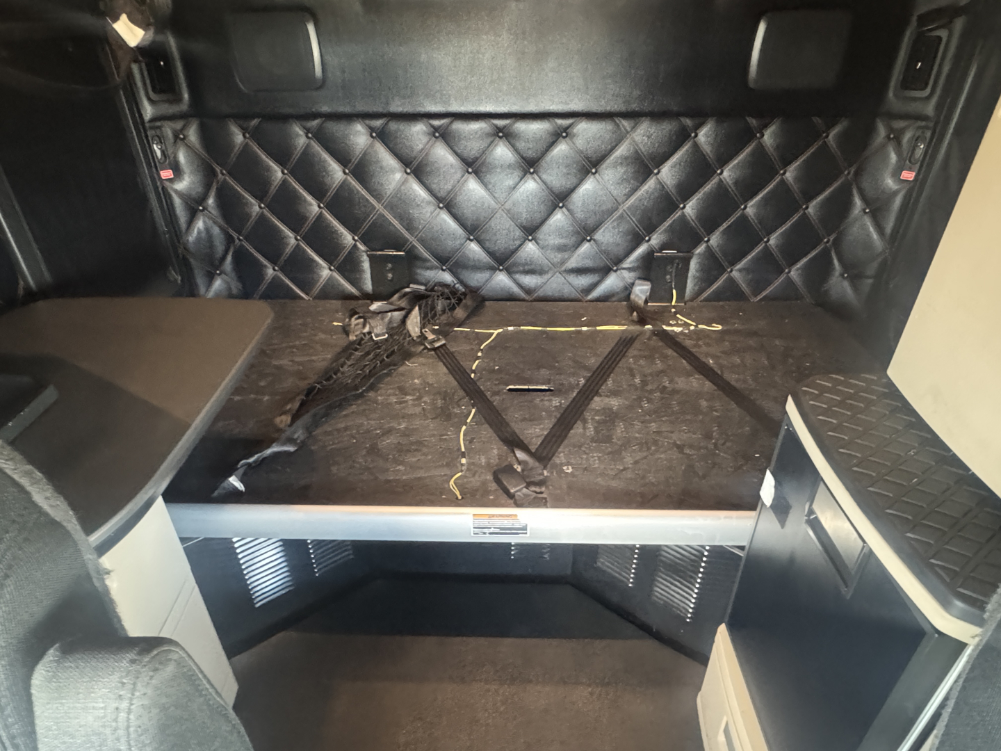 Kenworth T680 truck interior cargo area with diamond-stitched black upholstery on the wall, storage shelves, and cargo area with straps. Visible are no explicit model badges or numbers in the image.
