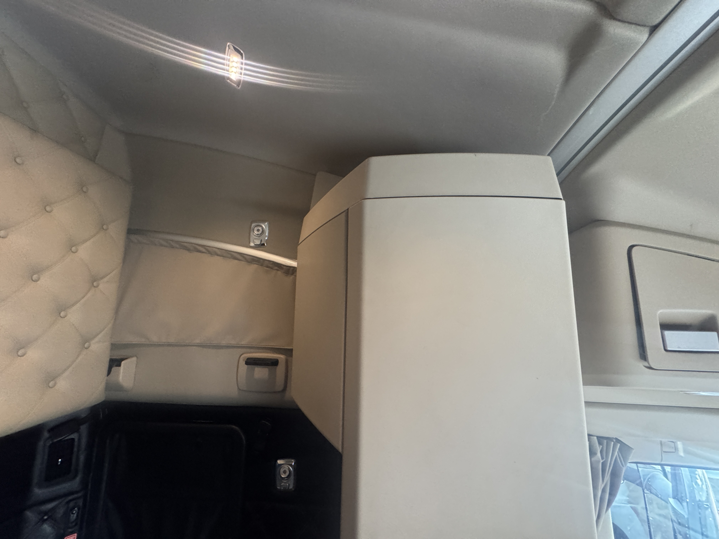 Kenworth T680 interior cab area with light gray upholstery, center console, and side storage; visible upholstery stitching and small control panels.