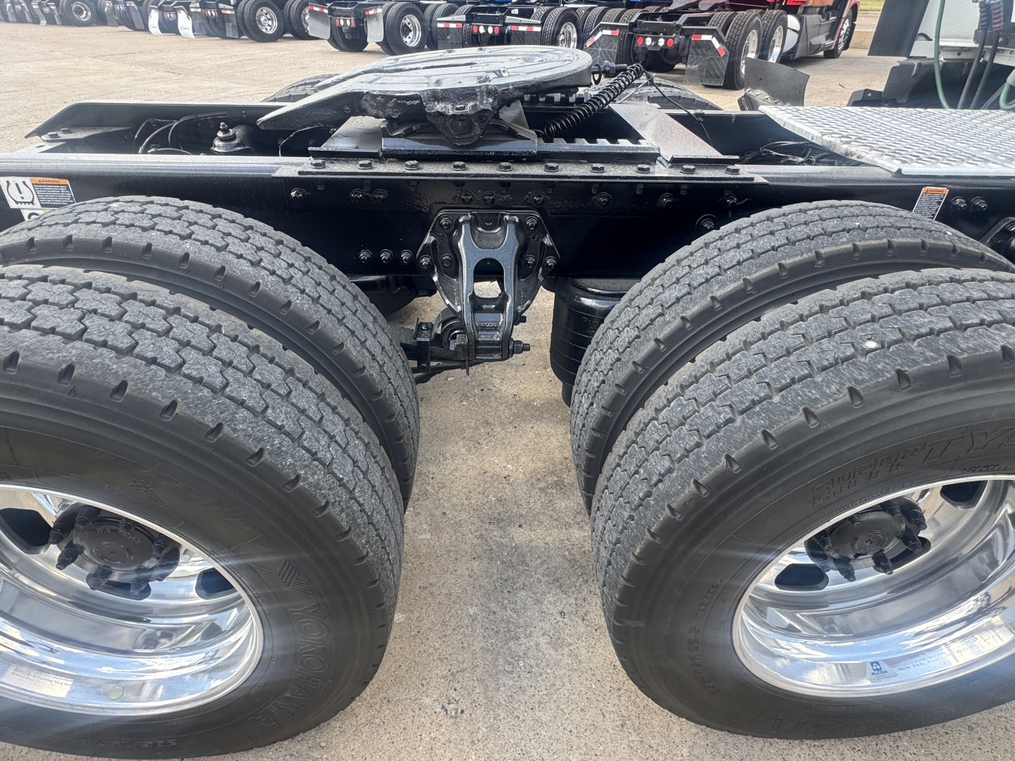 Kenworth T680 rear dual-axle setup showing two large tires and wheel rims, hitch/frame area and suspension components visible.