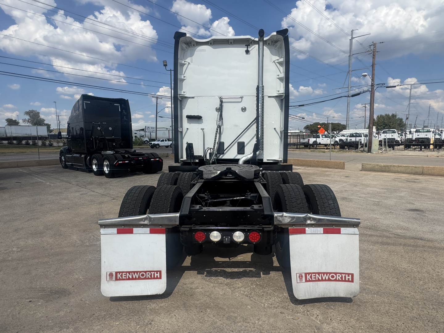 Kenworth T680 rear view showing chassis and dual rear axles with white mud flaps labeled Kenworth, under a clear sky.