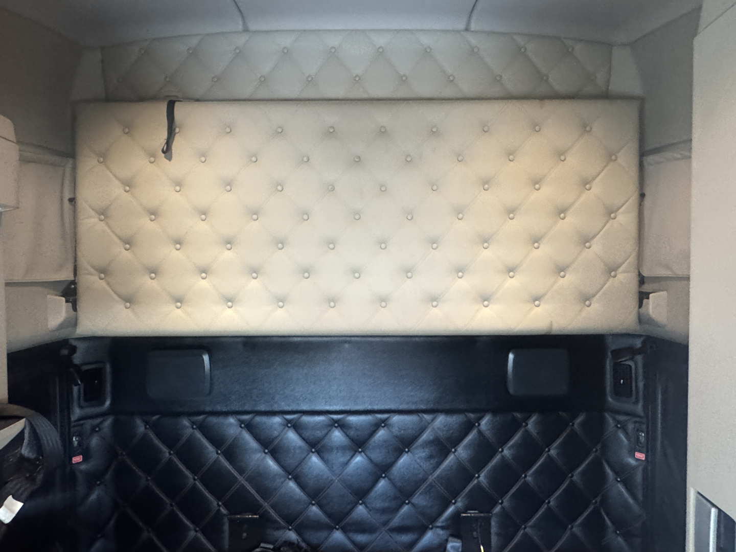 Kenworth T680 sleeper cab interior back wall with quilted upholstery panels and tan headboard visible.