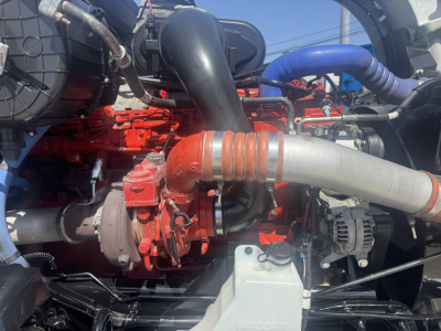 Kenworth T680 engine bay showing red engine components with hoses and a large gray intake pipe.