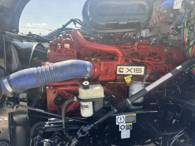 Kenworth T680 engine bay showing red Cummins X15 engine and blue coolant hose with attached filters and wiring harnesses.