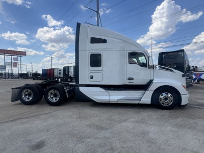 Side view of a white 2023 Kenworth T680 sleeper cab truck with multiple axles at rear, showing cab doors and windows.