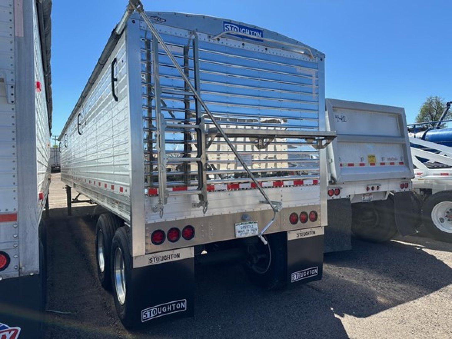 Stoughton air ride grain trailer rear view showing hinges, ladder, bumper, and Stoughton branding with mud flaps and reflective tape.