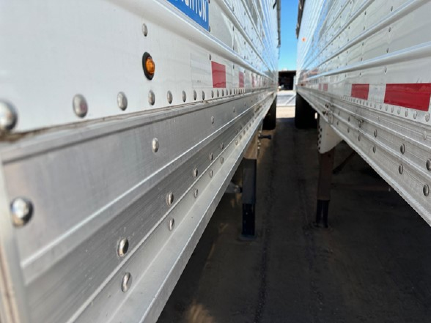 Trailer side view showing gap between two silver grain trailers with riveted panels and small reflective markers.