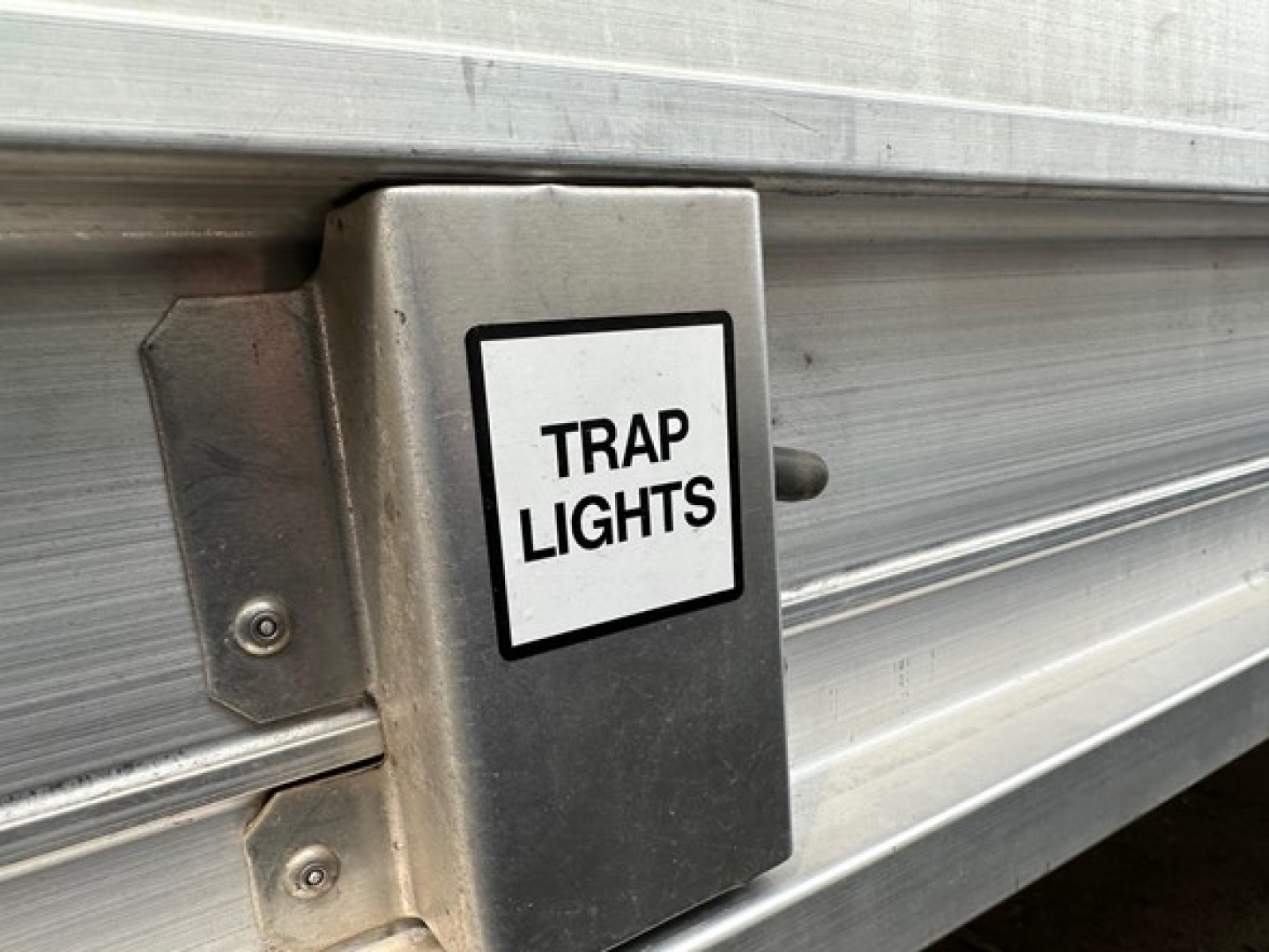 Trailer side with metal box labeled Trap Lights mounted on silver hopper side.