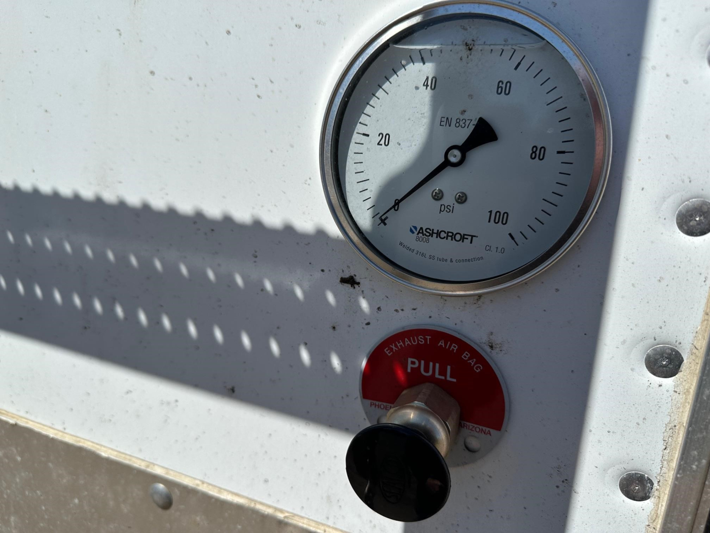 Gauge reads 0-100 psi with ASHCROFT label, adjacent red pull handle labeled EXHAUST AIR BAG PULL on a Stoughton grain trailer trailer door panel.