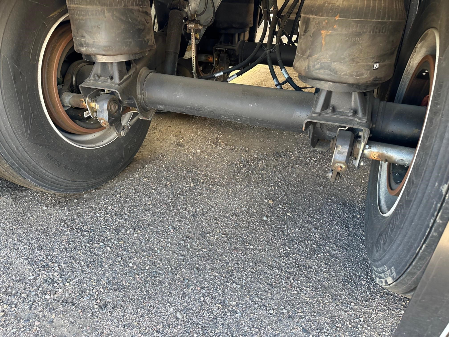 Rear view of a Stoughton grain trailer suspension showing a solid steel axle, leaf springs, and dual tires.
