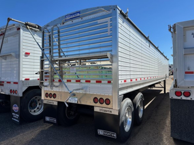 Stoughton air ride grain trailer in a lot, side view showing aluminum hopper with ribbed sides, rear discharge gate, dual rear axles, mud flaps reading SToughton, and small VIN/stock tags.