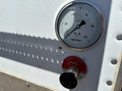Close-up view of a PSI pressure gauge on a metal trailer wall with an Ashcroft gauge showing 0-100 PSI and a red pull ring labeled Exhaust Air Bag.