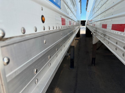 Trailer side view showing gap between two silver grain trailers with riveted panels and small reflective markers.