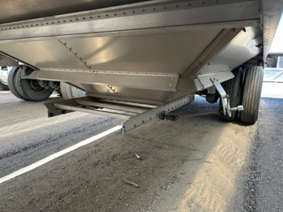 Trailer underside showing hopper grain trailer landing gear and suspension; steel beams, hinges, and a reinforced hopper bottom visible.