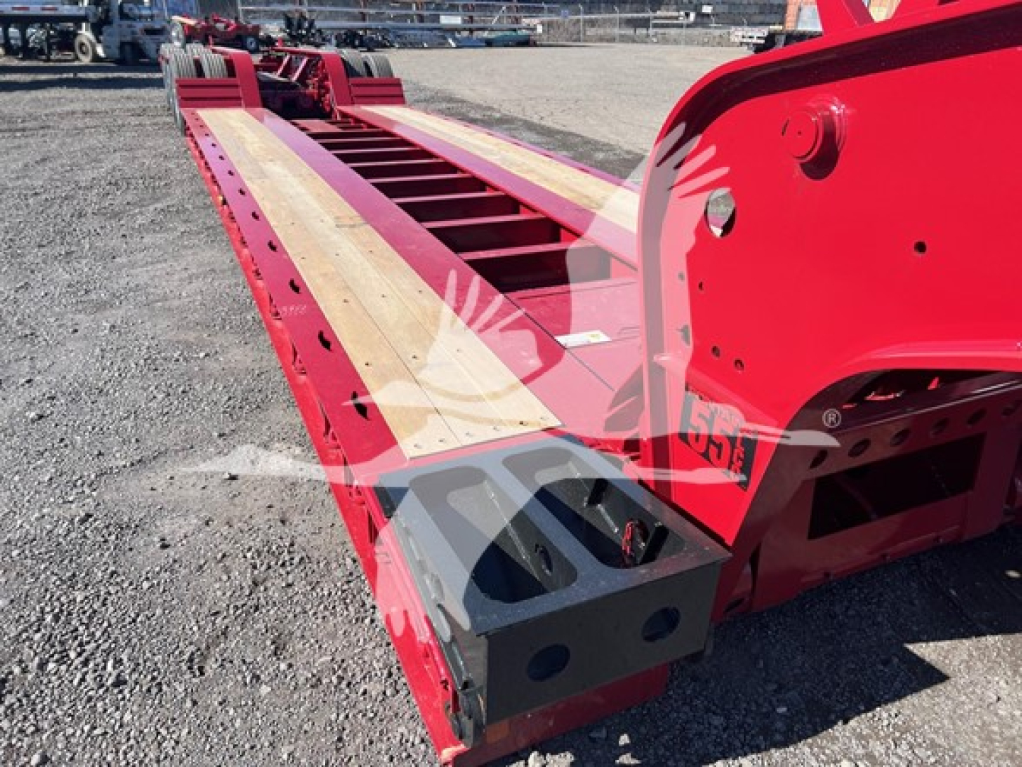Fontaine 55 Lcc lowboy trailer showing red frame and wooden deck with stake pockets and wheel chocks visible.