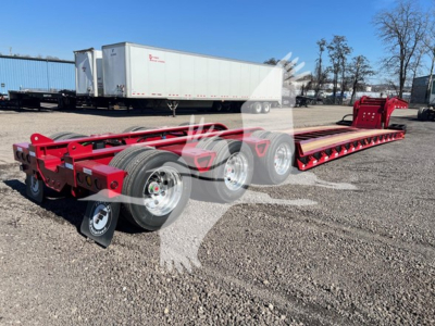 Trailer chassis showing a red Fontaine lowboy step deck with tandem axles and long flatbed, no text visible on side, gravel lot with other trailers in background.