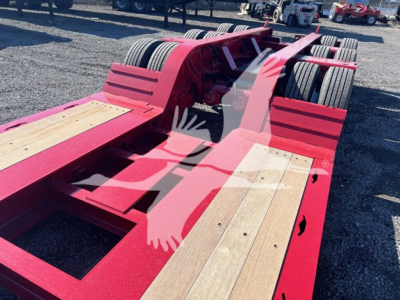 Fontaine lowboy trailer chassis showing red frame and wooden deck sections with dual rear axles.
