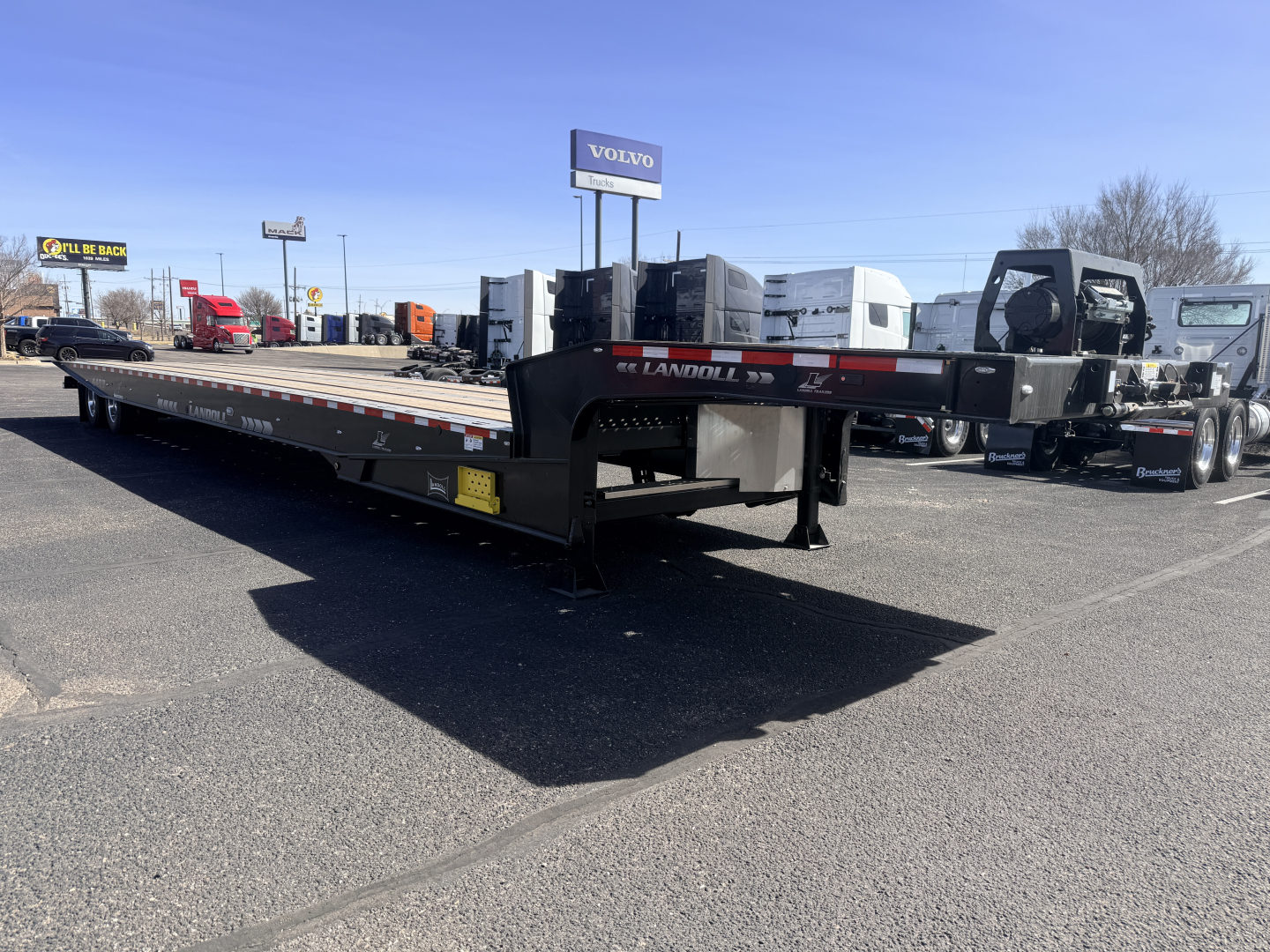 Landoll 440B-53 40-ton traveling axle lowboy trailer viewed from side-loading area with tractor in background and Volvo signage