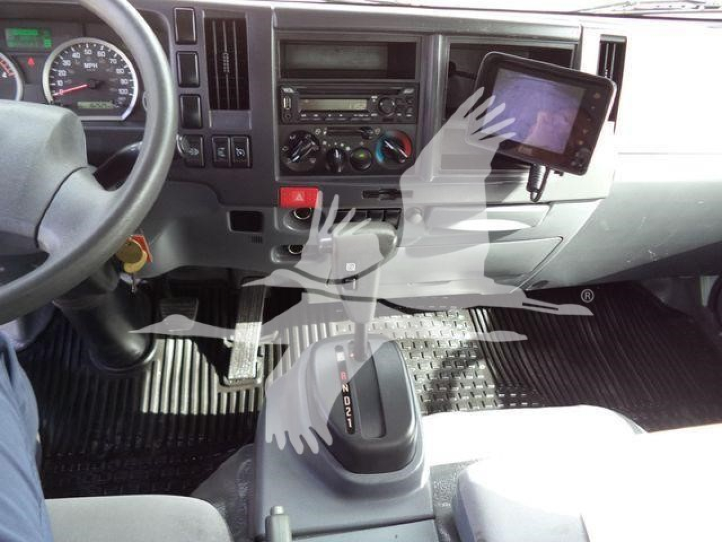 Isuzu NPRHD cab interior showing steering wheel, dashboard, gear shifter, and tablet dash mount with vehicle controls.