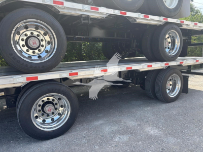 Trailer axle and wheels on a drop deck trailer, polished chrome rims, tires, and undercarriage visible with double stacked decks.