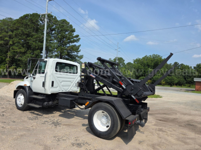 International 4300 dump/haul truck with DT466 engine, white cab, black hydraulic bed, rear loading arm, side view.