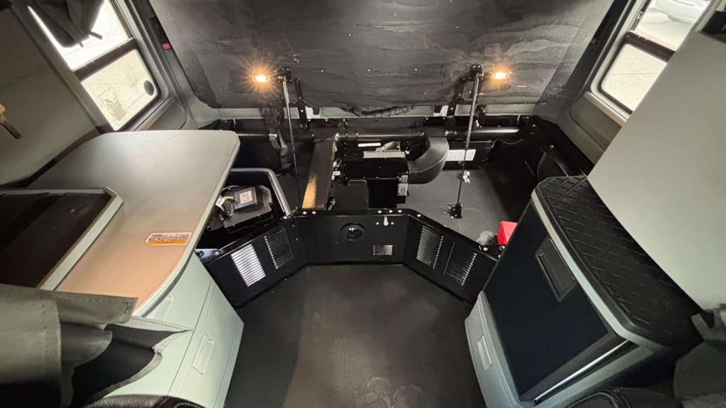 Cab interior of a 2022 Kenworth T680 shown from front, with dashboard removed and view of sleeper area and pedal box. No visible text legible.