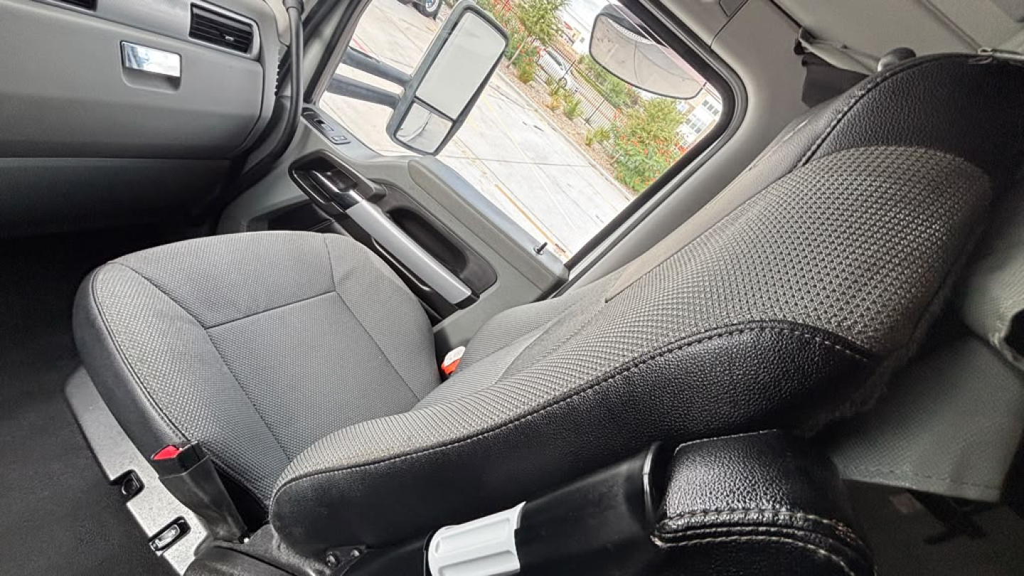 Truck cabin interior seat view showing driver seat and door with window, mirror, and controls.