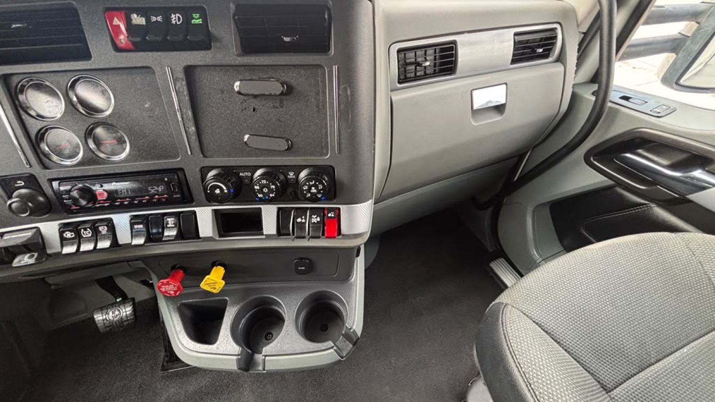 Kenworth T680 dashboard and center console area showing gauges, controls, storage, cup holders, and passenger seat.